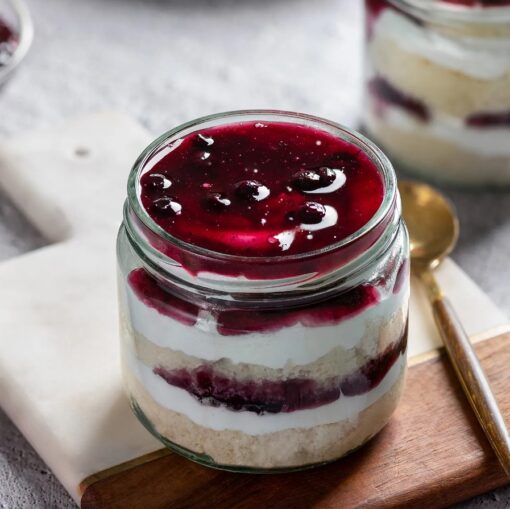 Two berry-flavored dessert jars with layered cake, cream, and berry compote in clear glass jars