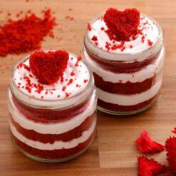 Set of six red velvet cake jars with cream cheese frosting and heart-shaped toppings in clear jars